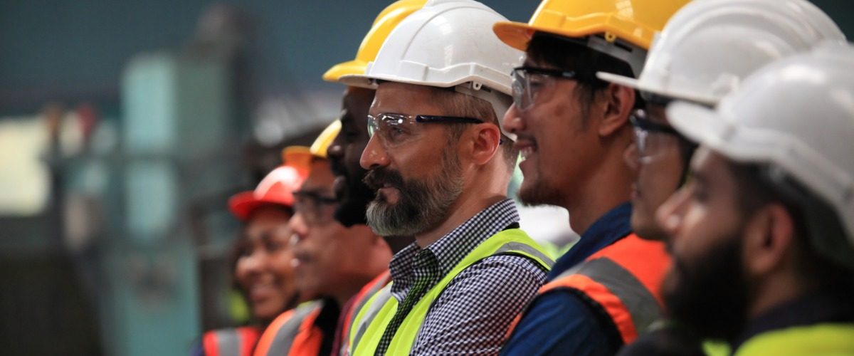 Several people are lined up. They are all wearing hardhats, protective eyewear, and high-visibility vests.