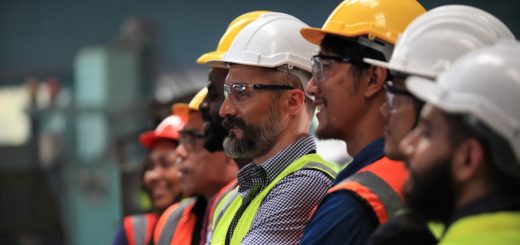 Several people are lined up. They are all wearing hardhats, protective eyewear, and high-visibility vests.