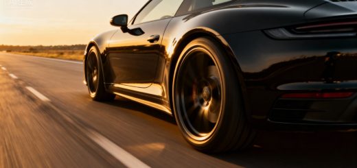 Low-angle rear view of a black luxury sports coupe speeding down a highway, illuminated by warm sunset light.