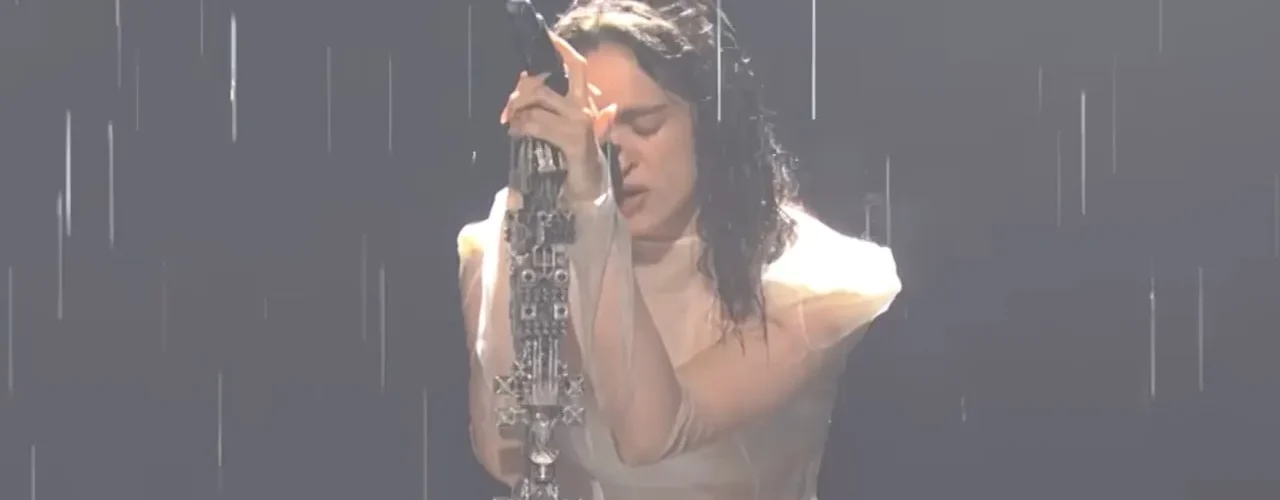 Rosalía performs “Magnolias” in the rain on SNL, head bowed against a microphone on an ornate stand