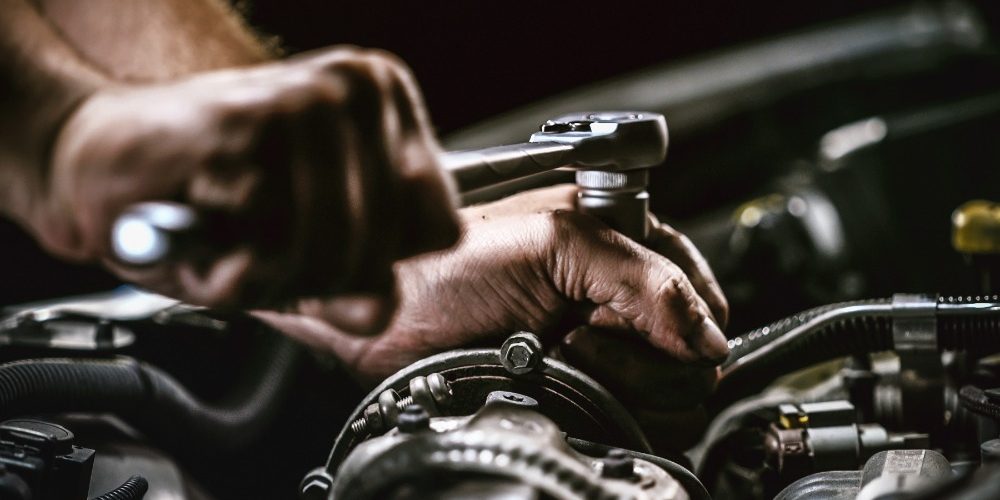 A person is working on a car engine. The person is using a wrench on the engine as he works on it.