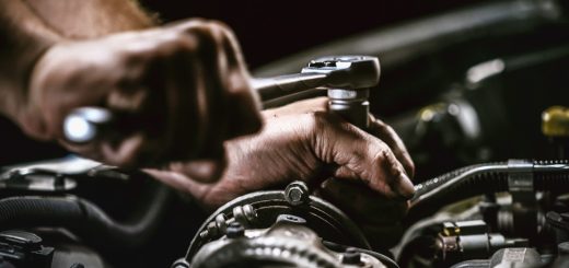 A person is working on a car engine. The person is using a wrench on the engine as he works on it.