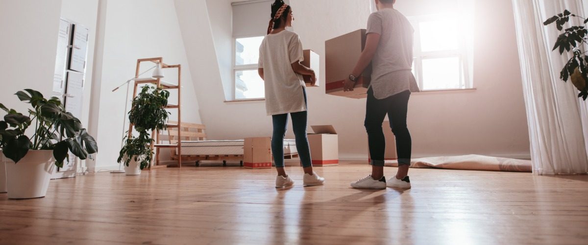 A man and a woman are standing in the middle of a living room. They are both holding boxes in their hands.