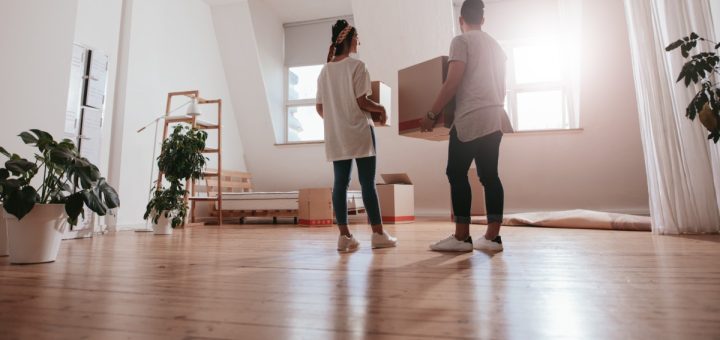 A man and a woman are standing in the middle of a living room. They are both holding boxes in their hands.