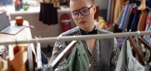 A person wearing glasses examines clothing on a rack filled with assorted garments inside a clothing store.