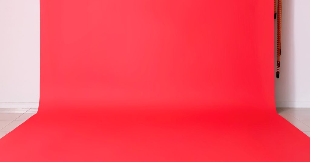 A vibrant red photo backdrop hanging against a white wall all the way down to the floor in a brightly lit room.