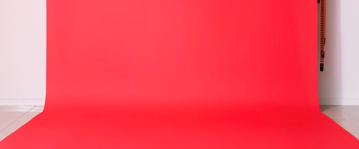 A vibrant red photo backdrop hanging against a white wall all the way down to the floor in a brightly lit room.