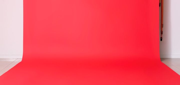 A vibrant red photo backdrop hanging against a white wall all the way down to the floor in a brightly lit room.